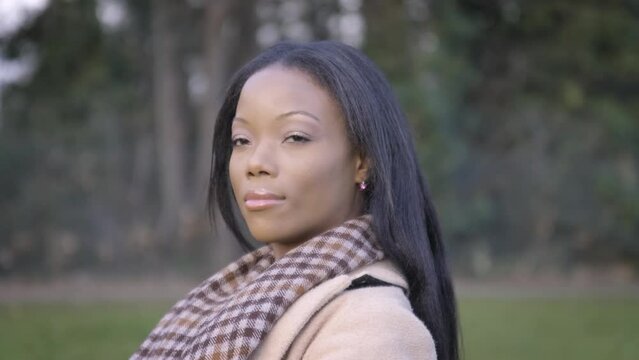 Attractive black woman turning head looking sitting on bench in park cloudy cold day central London. Slow motion 60fps 4K.