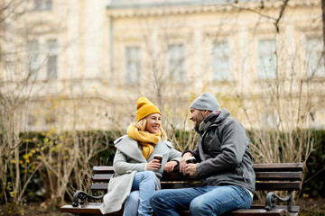Couple drinking hot beverage sitting on park bench in the winter outdoors