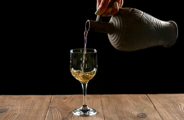 girl hands pouring red wine into a glass from a clay bottle on a black background