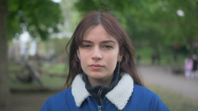 Brunette woman in denim jacket looking seriously at the camera in a park in slow motion