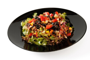 Delicious salad with lettuce, red pepper, tomato, corn and sliced olives on a black plate