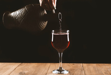 girl hands pouring red wine into a glass from a clay bottle on a black background