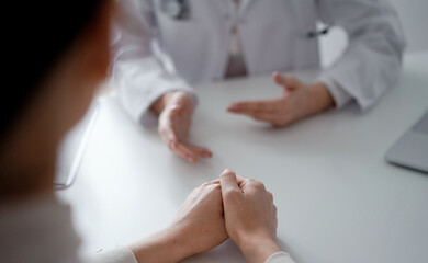 Obraz premium Doctor and patient discussing current health examination while sitting at the desk in clinic office. The focus is on female patient's hands, close up. Medicine concept.