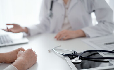 Doctor and patient sitting and discussing something at the desk in  clinic. The focus is on the stethoscope lying on the table, close up. Medicine and healthcare concept