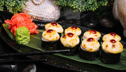 Served warm sushi rolled in nori sheets with ginger and wasabi on a black stone plate
