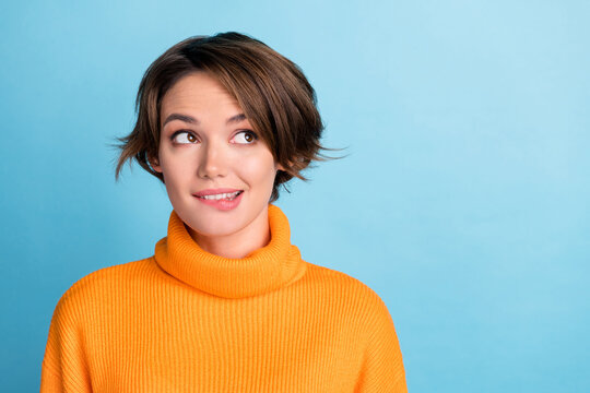 Photo of cheerful cute person biting lips look interested empty space isolated on blue color background