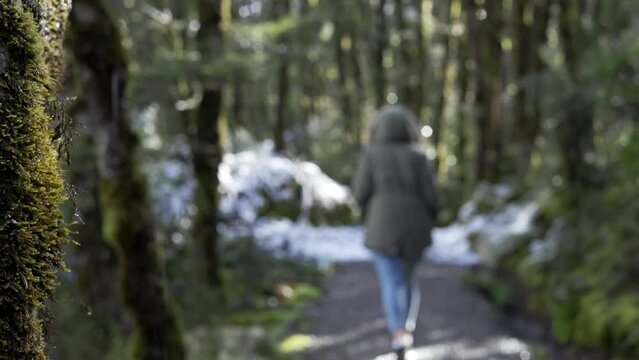 Woman walking on snowy trail among the deep forest.