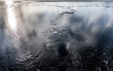 The texture of thin melting ice on a spring lake with the sky reflected on the surface. Light glare.