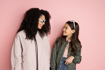 Smiling preteen girl in sunglasses looking at mom on pink background.