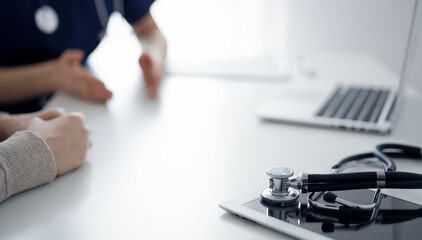 Stethoscope lying on the tablet computer in front of a doctor and patient at the background. Medicine, healthcare concept.