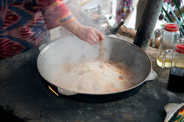 Cooking Uzbek pilaf in a cauldron in the summer kitchen in the courtyard of a private house. Bukhara. Uzbekistan