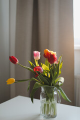 Fresh spring colorful bouquet of tulips in vase standing on white table in light classic design living room background. Festive flowers for gift. Mockup for greeting card