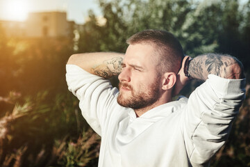 Portrait of young bearded man with tattoos in white jacket in countryside