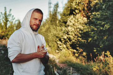 Naklejka na ściany i meble Portrait of young bearded man with tattoos in white jacket in countryside
