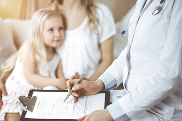 Doctor and patient. Pediatrician using clipboard while examining little girl with her mother at home. Happy cute caucasian child at medical exam. Medicine concept.