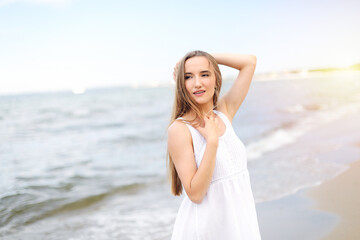 Fototapeta na wymiar Happy smiling woman in free happiness bliss on ocean beach standing straight. Portrait of blonde multicultural female model in white summer dress enjoying nature during travel holidays vacation