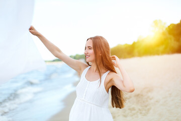 Happy smiling woman in free happiness bliss on ocean beach catching clouds. Portrait of a multicultural female model in white summer dress enjoying nature during travel holidays vacation outdoors.