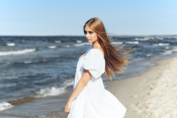 Fototapeta na wymiar Happy, beautiful woman on the ocean beach standing in a white summer dress. Portrait.