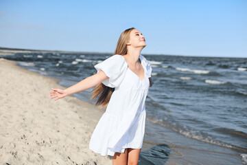 Happy smiling beautiful woman is on the ocean beach in a white summer dress, open arms.