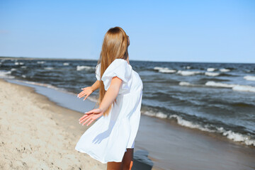 Fototapeta na wymiar Happy smiling beautiful woman is on the ocean beach in a white summer dress, open arms.