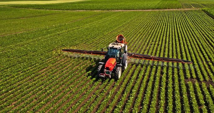 Farmer in tractor spraying pesticide on industrial soybean field
