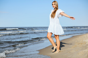 Fototapeta na wymiar Happy smiling beautiful woman is walking on the ocean beach with open arms.
