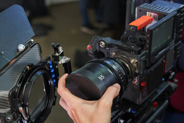 Fototapeta na wymiar A caucasian videographer's hand installs an 85mm lens on a professional movie camera