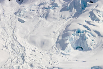 Snow covered mountain slope, Antarctic Peninsula. Rocks exposed on snowy slope. Blue ice visible; opening to ice cave.
