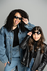 Fashionable parent and daughter posing with sunglasses isolated on grey.