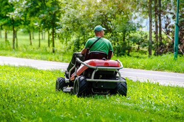 A man on a lawn mower in a summer park - obrazy, fototapety, plakaty