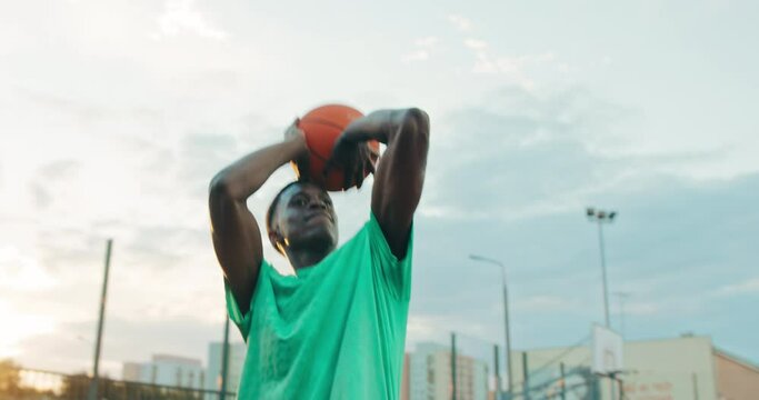 Handsome african american man in sportswear fashionable stylish playing basketball at blayground with firends spends time together in good mood . Guy does slam dunk.