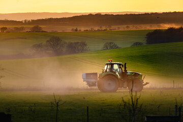 Tractor in farmland working on soil field with sunset, big equipment, countryside scene