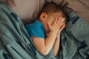Close up on single boy rubbing his eyes with both hands while he is in bed for sleeping 