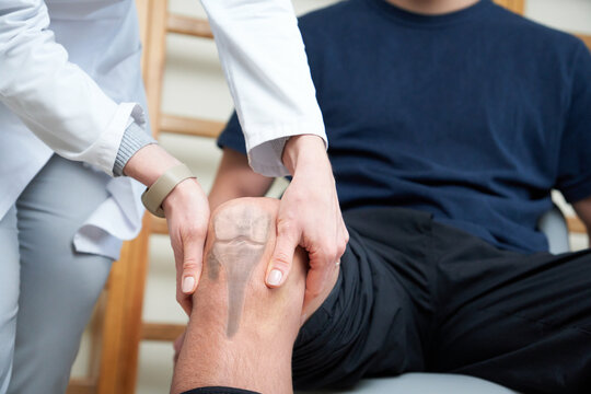 Young doctor neurologist examining her patient. Pretty female orthopedist with patient in her office. Neurologist checks the reflexes of a young age male patient.
