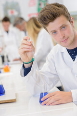 Male science student holding pipette and glass flask