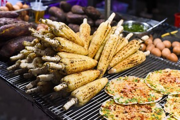 Grilled corn near vietnamese pancake with eggs, sausages and sauces in vietnamese night market in...