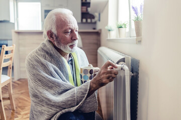 Men's hand adjusting thermostat valve of heating radiator in the bedroom. Senior men adjusting the...