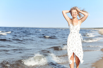 Fototapeta na wymiar Happy blonde beautiful woman having fun on ocean beach while dancing in waves.