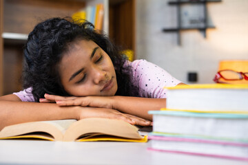 Tired young indian student sleeping on table during reading for examination at home - concept of...