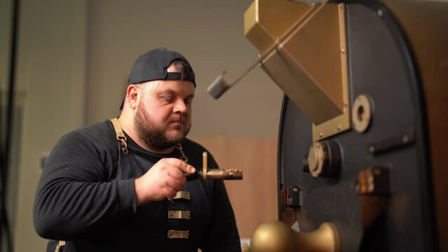 Male worker in apron smelling coffee on sampler spoon