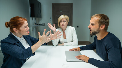 Blond, red-haired woman and bearded man in suits in the office. Business people are swearing during...