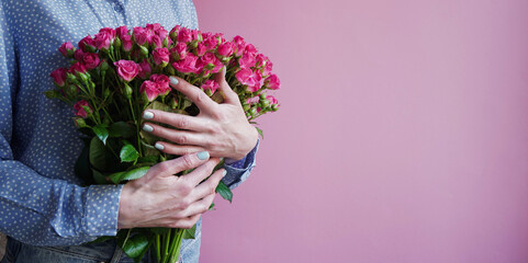 International Women's Day.Concept of greeting banner for international women's day on March 8.Close-up girl's hands holding large bouquet pink roses on pink background,copy space. Mother's day banner.
