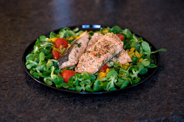 ready to eat - lamb's lettuce, cherry tomatoes, yellow paprika, herbs and roasted salmon on a black plate