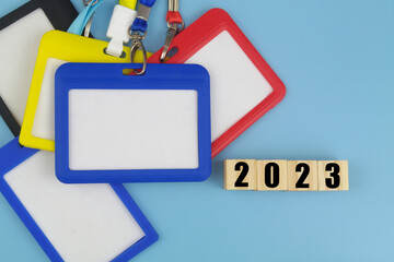 Many blank badges and numbers 2023 on wooden cubes on blue. Accreditation for events in year 2023 concept.