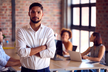 Portrait Of Businessman With Serious Expression Standing In Busy Office 