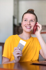 Portrait of happy girl, young positive pretty woman paying, holding credit bank card with phone, laptop. Online shopping at home in living room. Bank application, app.