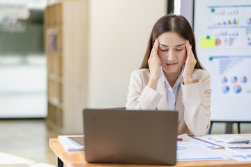 Female accountant having headache with overloaded work Stressed woman with headache working with laptop in office