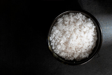 Sea salt crystals in bowl on black stone table.