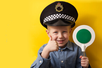 Cute boy in a cap of a policeman showing a thumbs up at a green traffic light on a yellow background