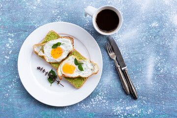 Breakfast food fried egg on bread avocado spread and coffee on blue wood table.